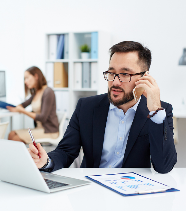 Person on phone with pen in hand looking at laptop office businessman